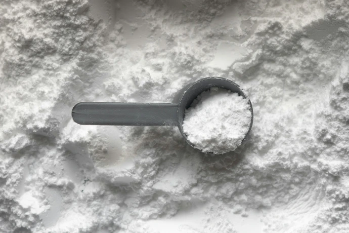 A grey plastic scoop filled with white powder resting on a pile of powder